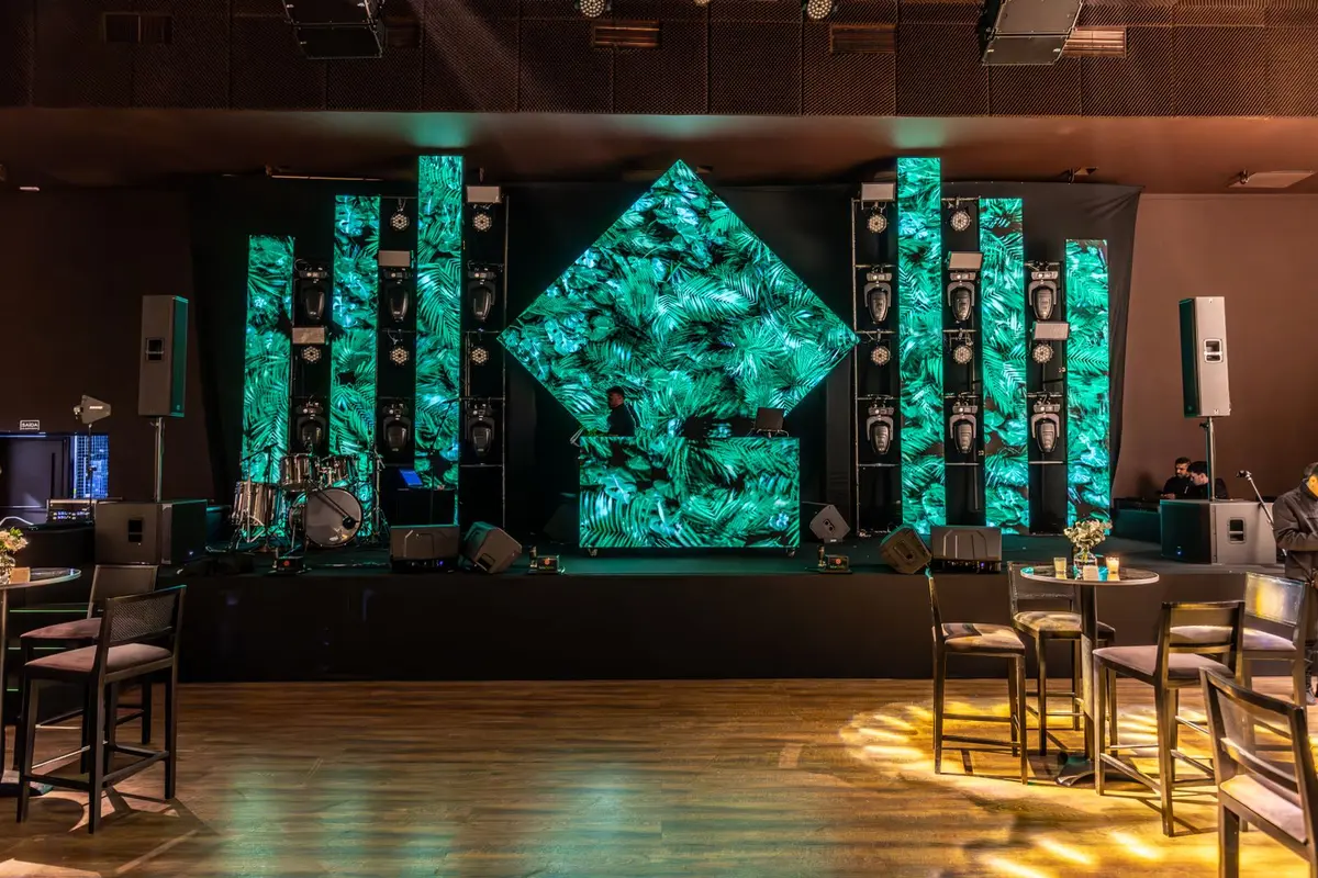 Escenario interior con pantalla central, columnas LED y cabina de DJ — imagen referencial